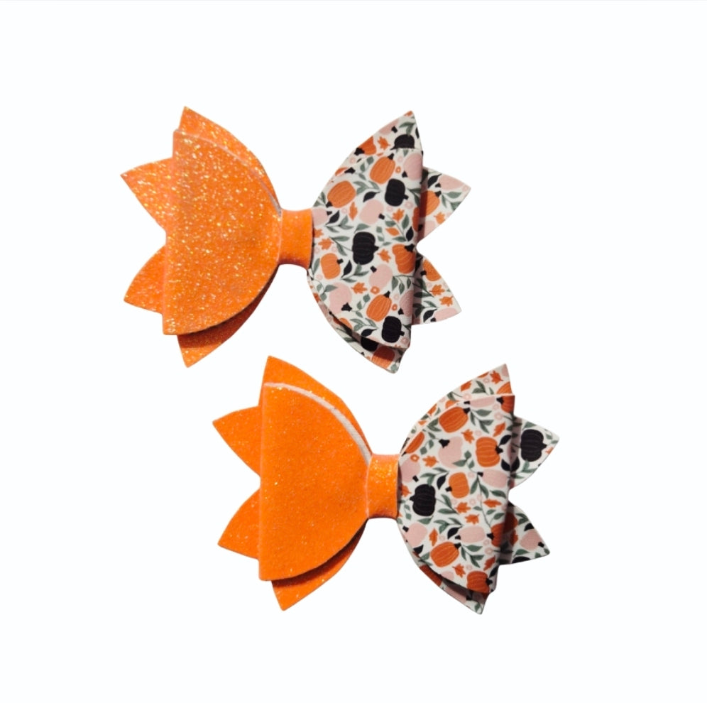 Handmade bright orange glitter faux leather Halloween hair bow set with pumpkin print for babies, toddlers, and girls.
