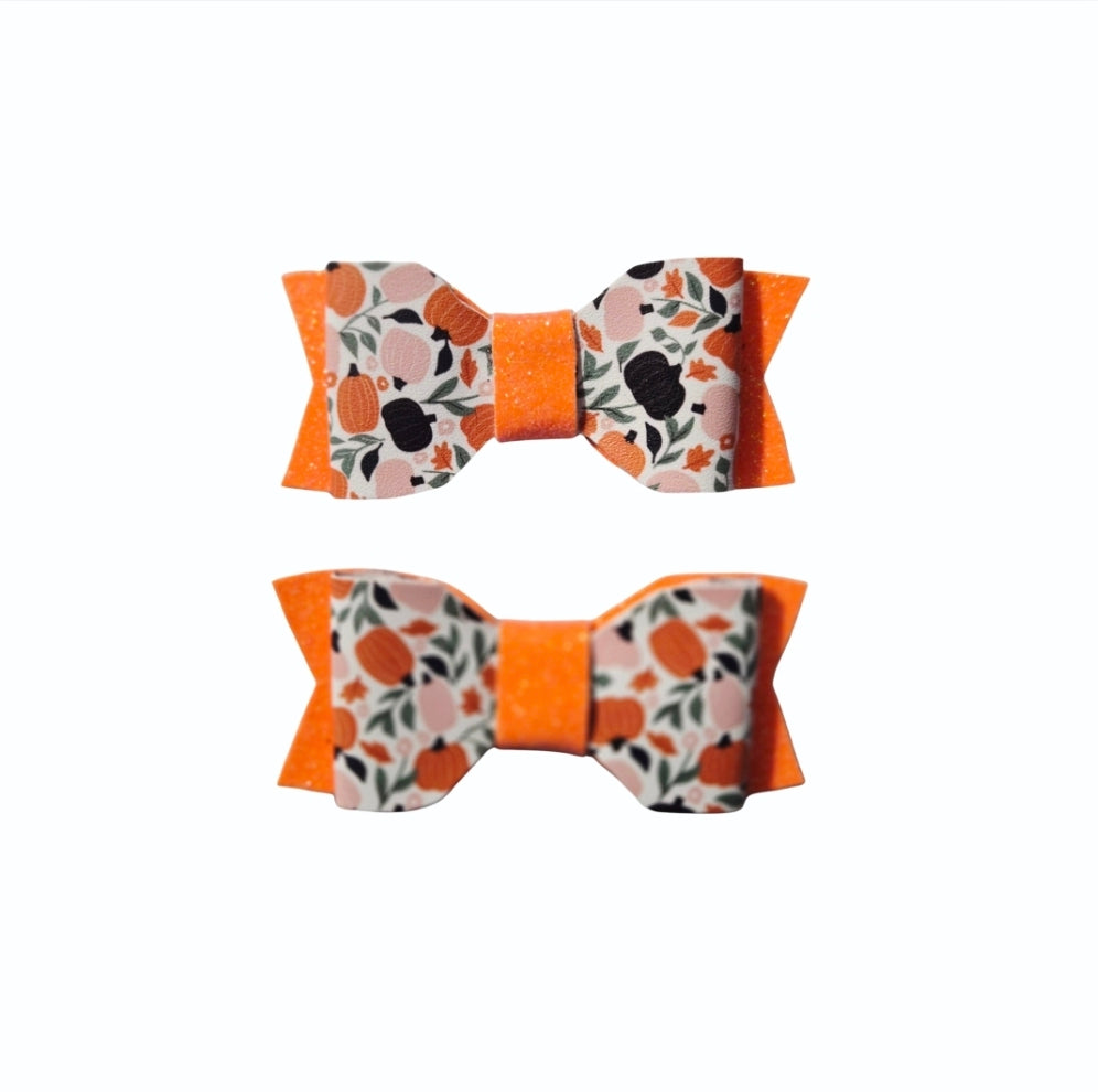 Handmade bright orange glitter faux leather Halloween hair bow set with pumpkin print for babies, toddlers, and girls.