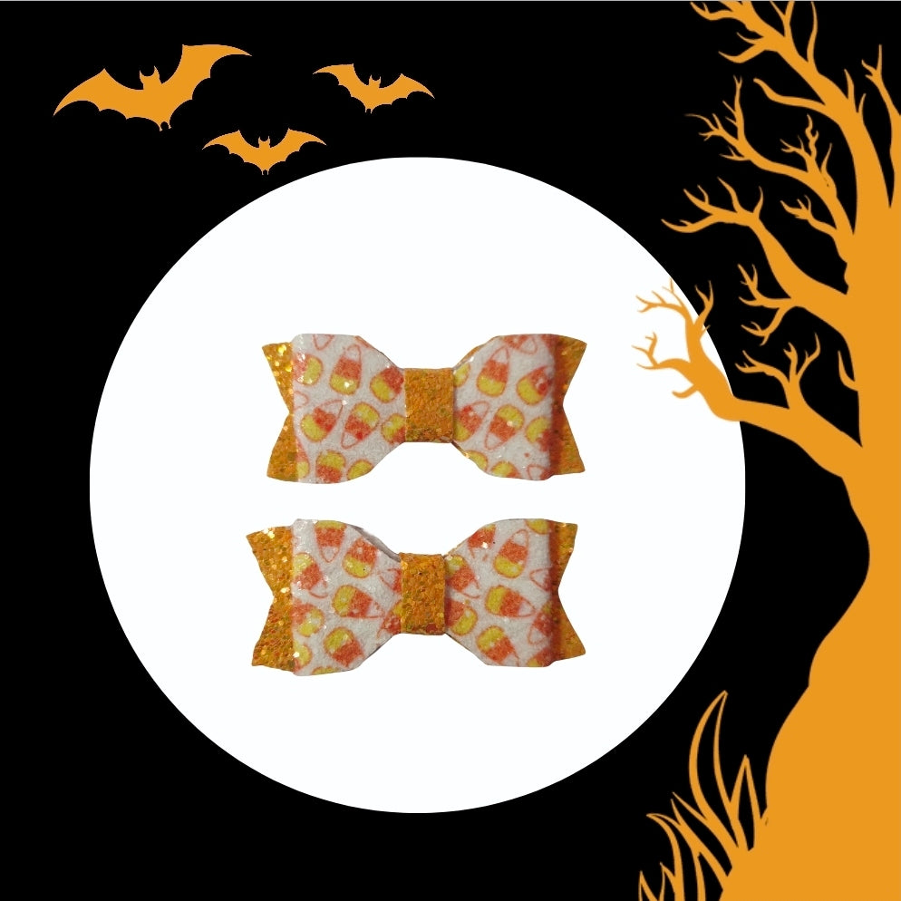 Close-up of handmade candy corn mini hair bows featuring glitter orange accents for Halloween and fall outfits.