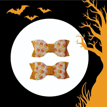 Close-up of handmade candy corn mini hair bows featuring glitter orange accents for Halloween and fall outfits.