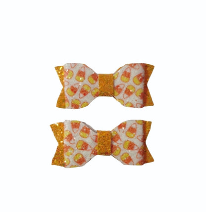 Two handmade candy corn mini hair bows with glitter accents for girls, perfect for Halloween outfits and spooky season.