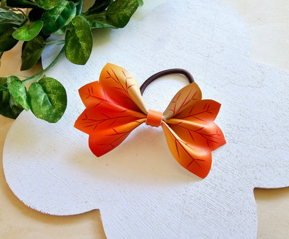 Handmade orange and yellow autumn leaf hair bow attached to a brown ponytail holder.