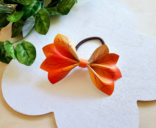 Handmade orange and yellow autumn leaf hair bow attached to a brown ponytail holder.