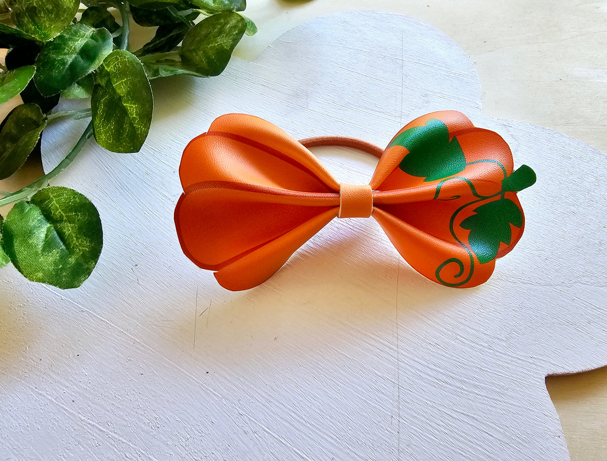 Orange and green pumpkin-inspired ponytail holder displayed on a white background.