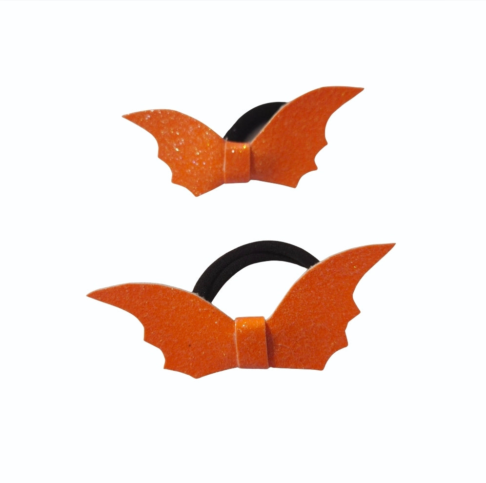 Close-up of a handmade glitter Halloween bat hair tie with orange bat wings and black ponytail holder.
