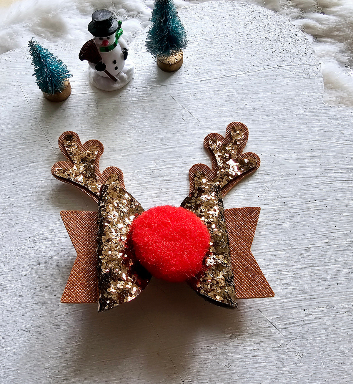 Handmade brown reindeer Christmas hair bow with glitter antlers, closed eyelashes, fluffy black nose and sparkling brown ribbon layers.