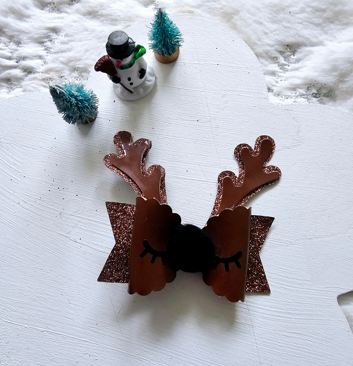 Handmade brown reindeer Christmas hair bow with glitter antlers, closed eyelashes, fluffy black nose and sparkling brown ribbon layers.