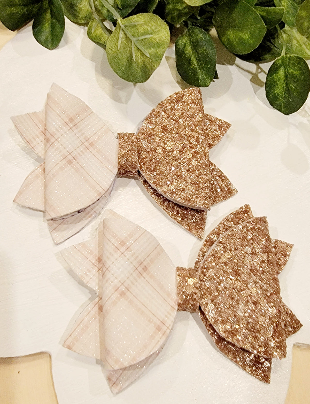 Two handmade girls' hair bows featuring cream almond plaid ribbon and sparkling champagne-gold glitter layers.