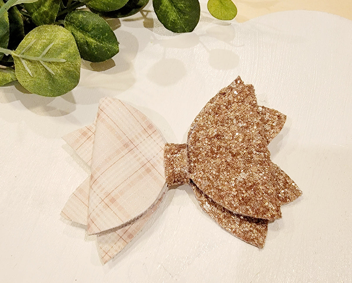 Close-up of a layered hair bow with soft cream plaid on one side and chunky gold glitter on the other.