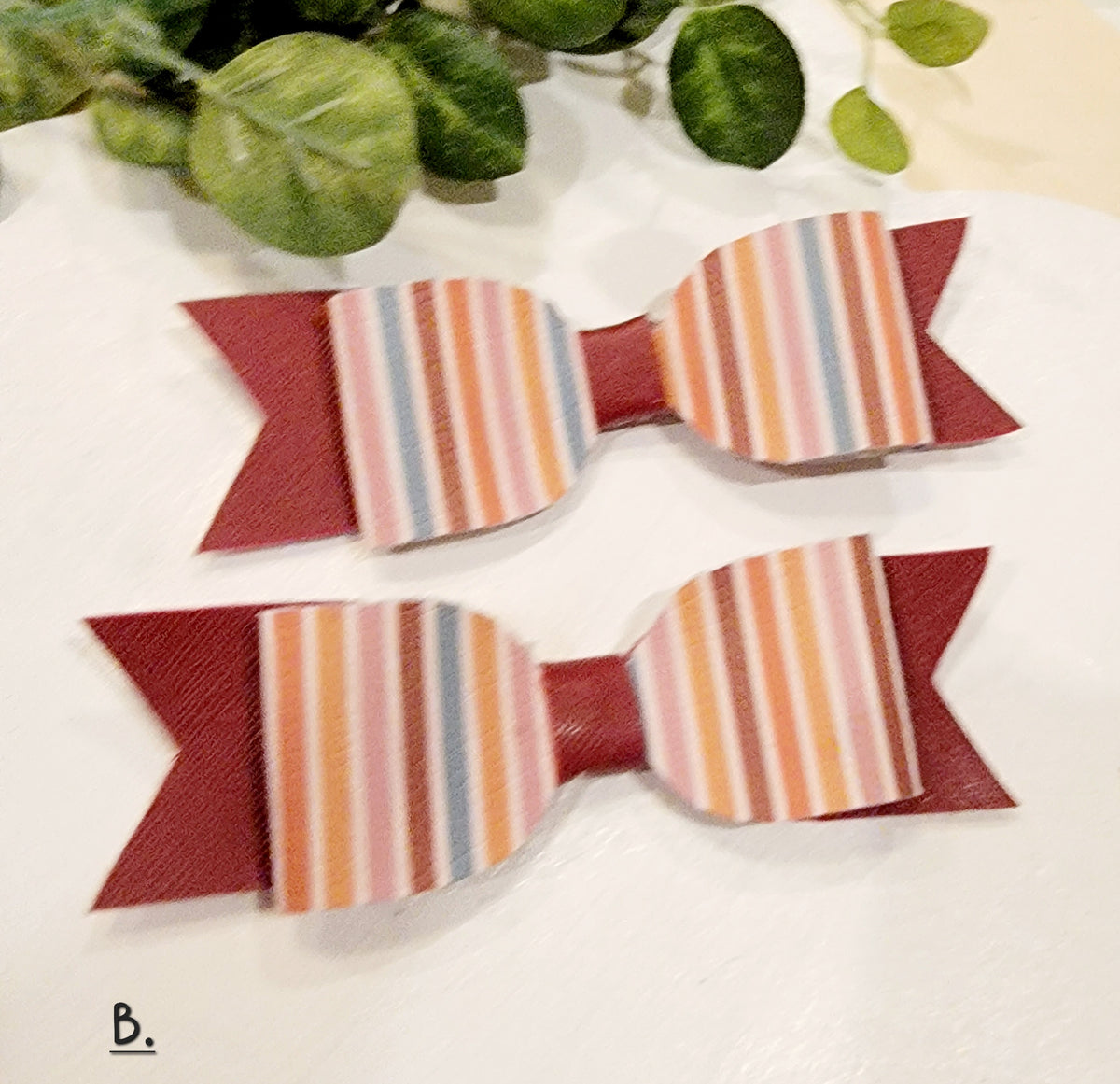 Two handmade girls' fall hair bows with multicolored striped fronts and burgundy ribbon backing.