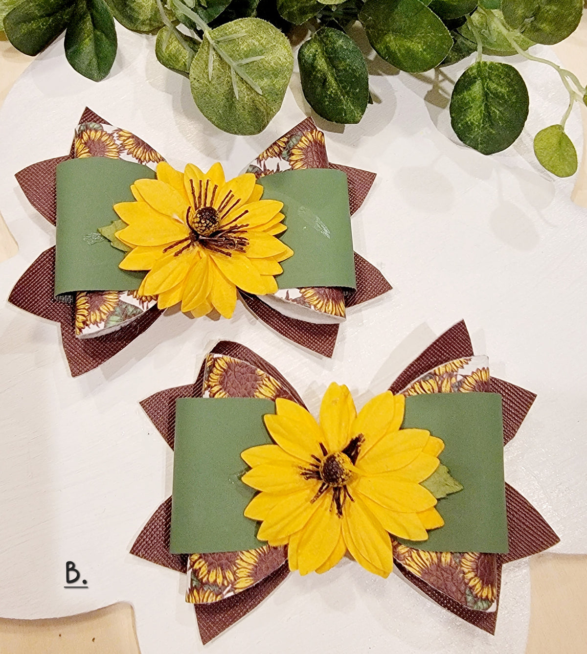 Two handmade sunflower hair bows with bright yellow flowers, green ribbon and brown patterned layers.