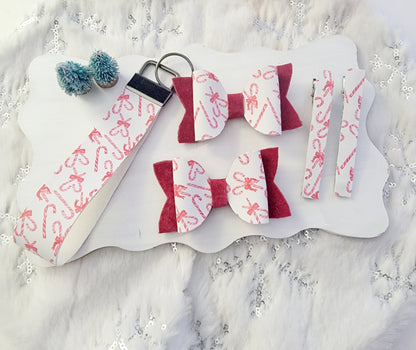 Two matching Christmas hair bows featuring white candy cane print fabric, red accents and festive holiday embellishments.