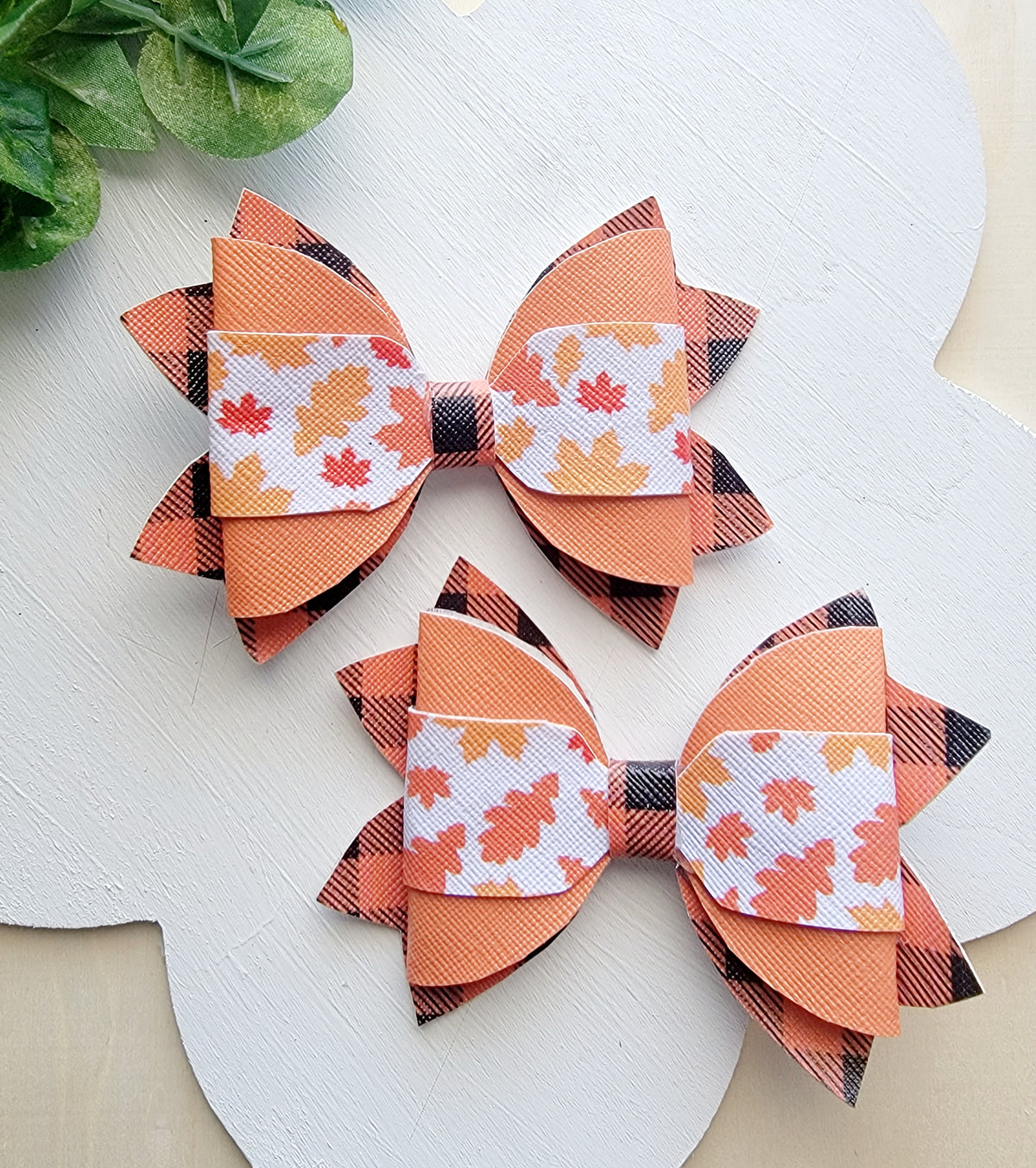 Two matching handmade hair bows featuring orange plaid ribbon and colorful autumn leaf patterns.