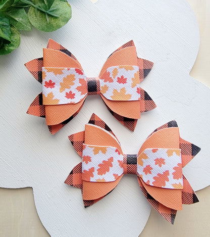 Two matching handmade hair bows featuring orange plaid ribbon and colorful autumn leaf patterns.