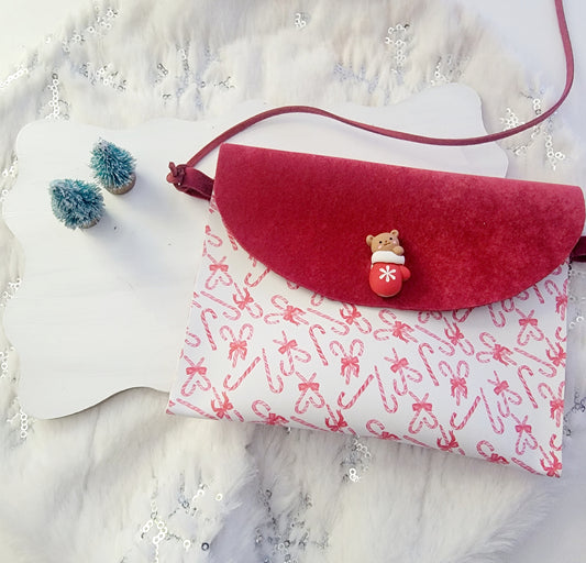Peppermint Christmas purse featuring a red flap, white fabric with red candy cane print, shoulder strap and holiday embellishment on a white display.