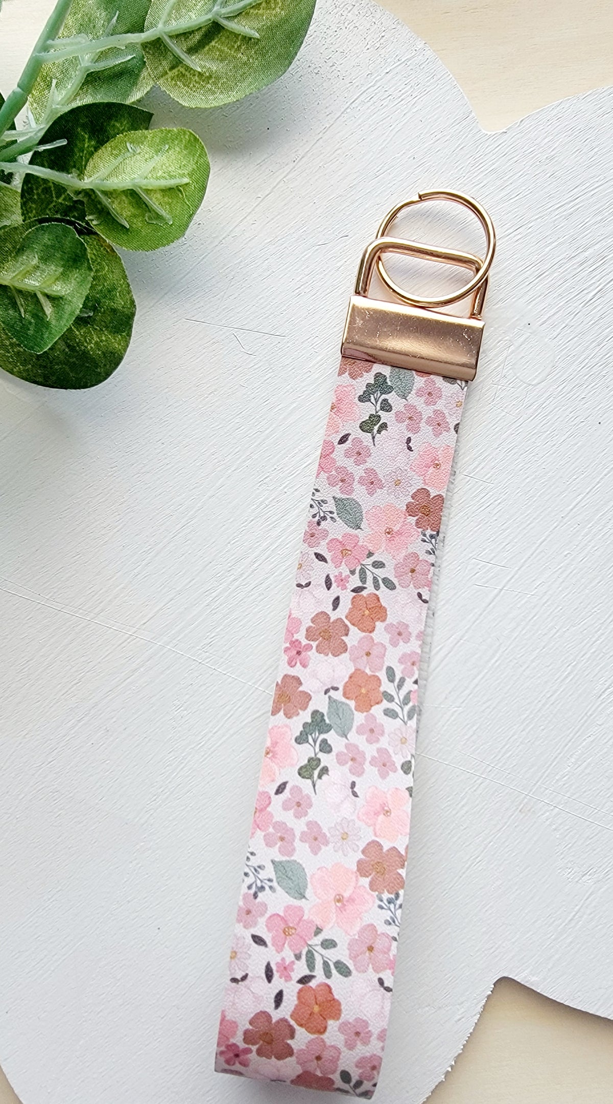 Handmade pink floral fabric wristlet with a gold-tone metal clasp displayed on a white background.