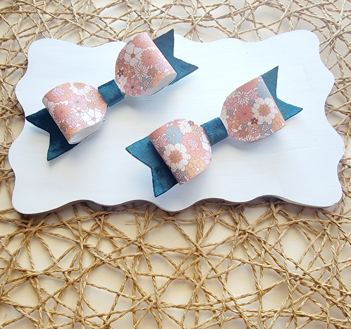 Pink floral faux leather hair bows with navy blue backing displayed together on a white board.