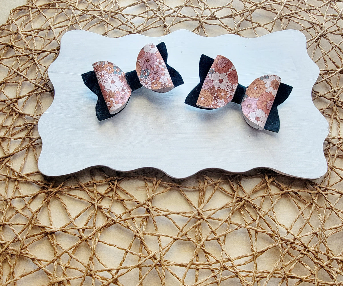Pink floral faux leather hair bows with navy blue backing displayed together on a white board.