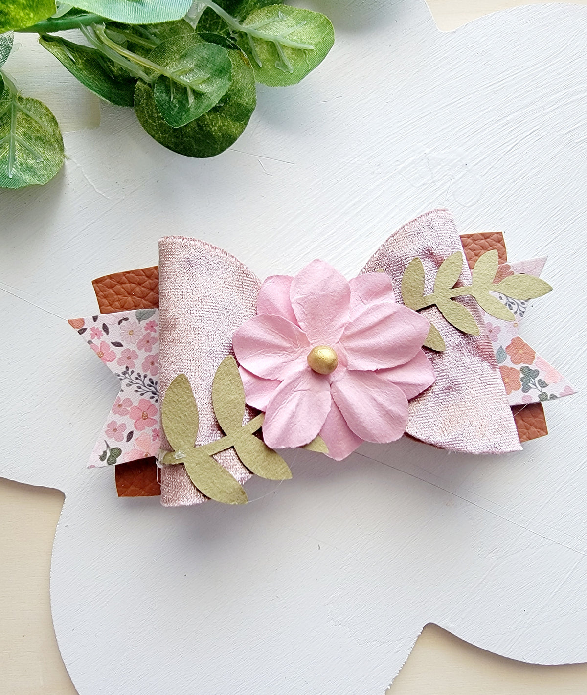 Close-up of a handmade pink layered flower hair bow with floral print, glitter accents and a pearl-like center.