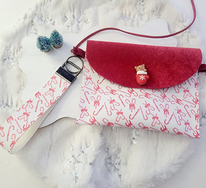 Red-and-white candy cane Christmas purse with red flap, festive embellishment and matching shoulder strap displayed on a snowy holiday background.