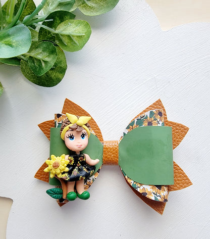 Handmade sunflower-themed hair bow with olive green faux leather, orange floral layers and a decorative sunflower girl centerpiece.